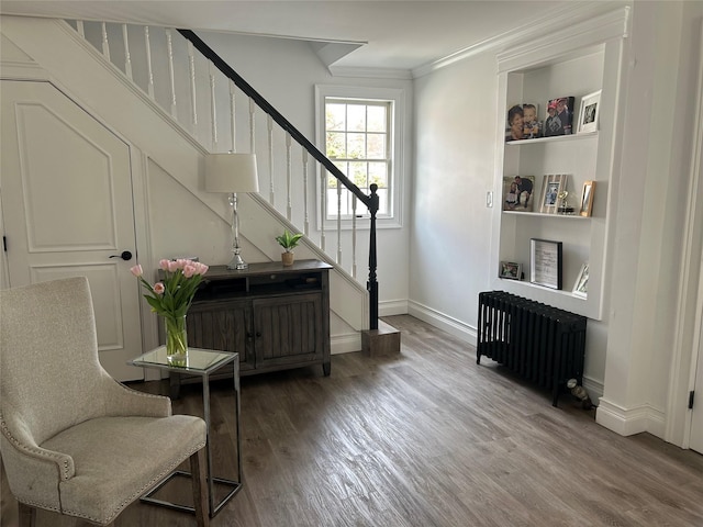 sitting room featuring radiator heating unit, baseboards, wood finished floors, and stairs