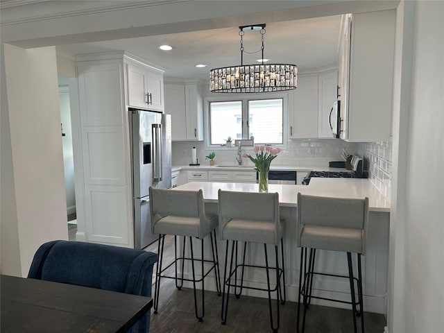 kitchen featuring dark wood-style floors, a sink, a peninsula, tasteful backsplash, and appliances with stainless steel finishes