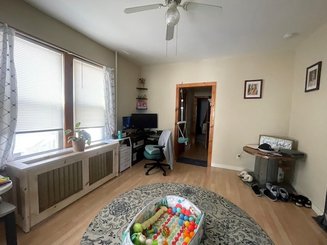office space with radiator heating unit, ceiling fan, light wood-type flooring, and baseboards