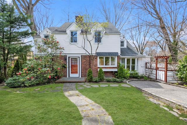 view of front of home with brick siding, a chimney, a front lawn, and fence