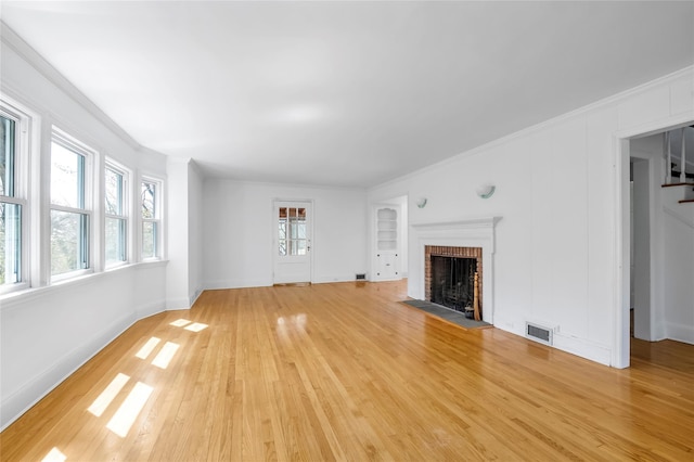 unfurnished living room featuring a brick fireplace, visible vents, light wood finished floors, and ornamental molding