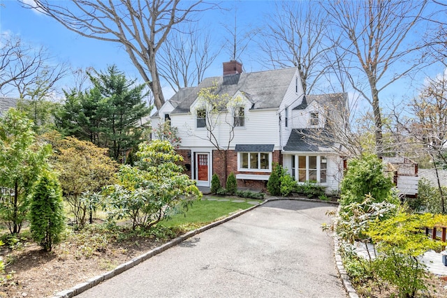 cape cod home with brick siding, driveway, and a chimney