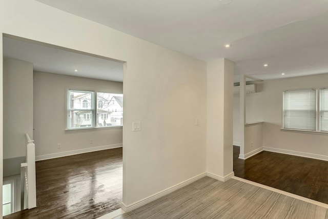 unfurnished room featuring an AC wall unit, baseboards, wood finished floors, and recessed lighting