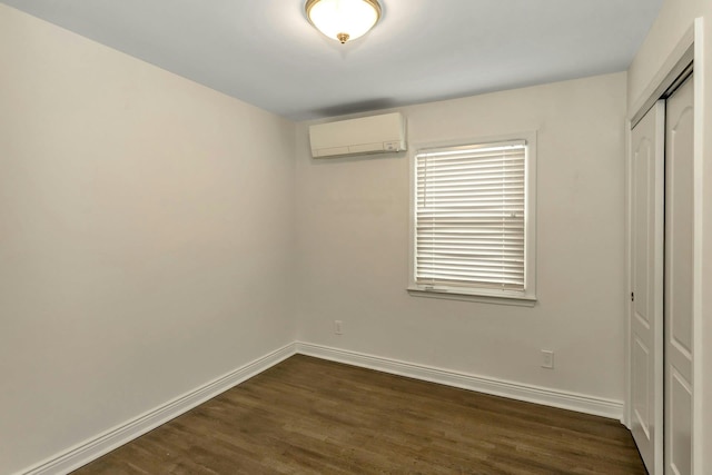unfurnished bedroom featuring baseboards, an AC wall unit, a closet, and dark wood finished floors