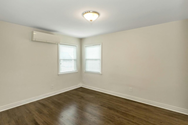 empty room featuring baseboards, a wall unit AC, and dark wood-style floors
