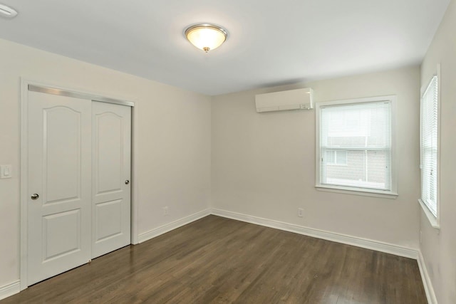 unfurnished bedroom featuring multiple windows, an AC wall unit, baseboards, and dark wood-style flooring
