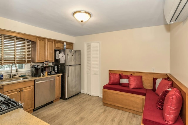 kitchen featuring an AC wall unit, a sink, light wood-type flooring, light countertops, and appliances with stainless steel finishes