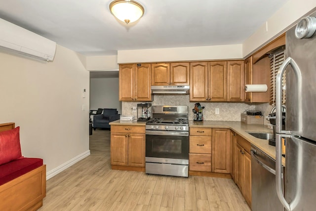 kitchen with decorative backsplash, a wall mounted AC, appliances with stainless steel finishes, light wood finished floors, and under cabinet range hood