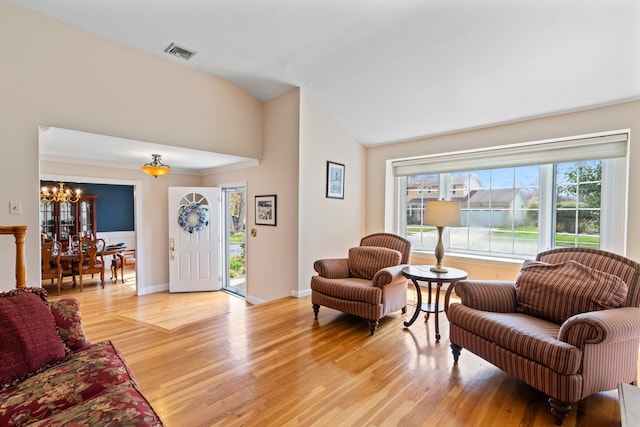 living area featuring a chandelier, vaulted ceiling, visible vents, and light wood finished floors