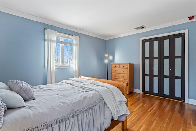 bedroom featuring visible vents, baseboards, wood finished floors, and ornamental molding