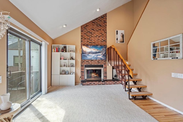 living room with baseboards, wood finished floors, a brick fireplace, stairs, and high vaulted ceiling