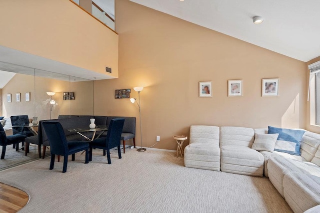 carpeted living area featuring high vaulted ceiling, baseboards, and visible vents