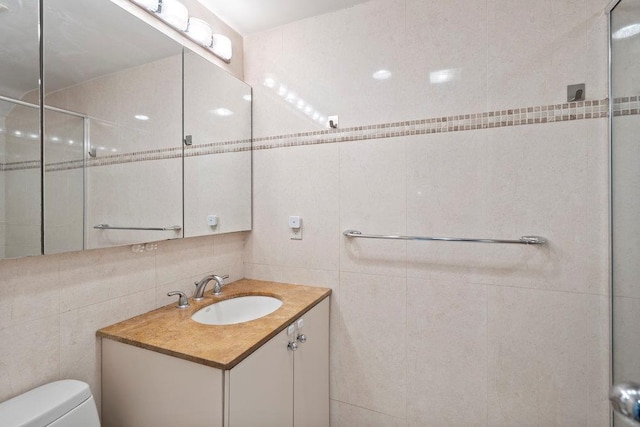 bathroom featuring a tile shower, toilet, vanity, and tile walls