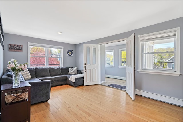 living room with a baseboard heating unit, baseboards, a wealth of natural light, and light wood-type flooring