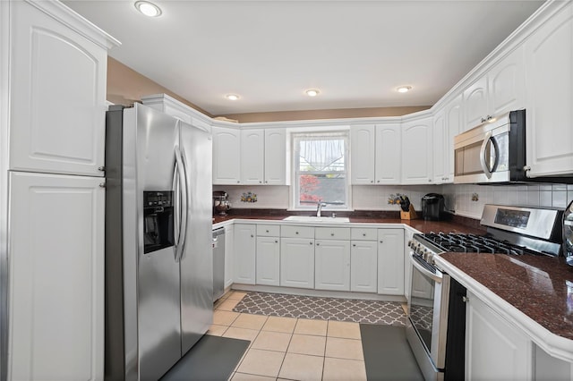 kitchen with light tile patterned floors, white cabinetry, a sink, dark countertops, and stainless steel appliances