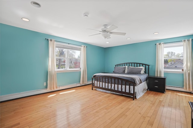 bedroom featuring baseboard heating, hardwood / wood-style flooring, and multiple windows
