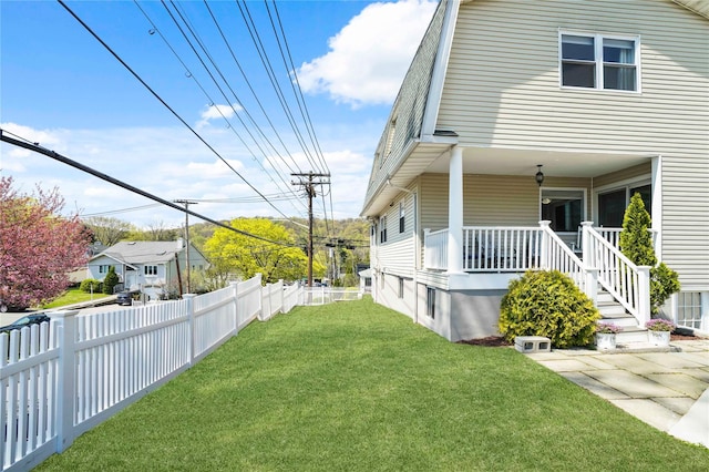 view of side of home with a lawn, covered porch, and fence