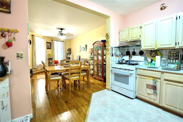 kitchen featuring a ceiling fan, light wood-type flooring, light countertops, under cabinet range hood, and white gas range oven