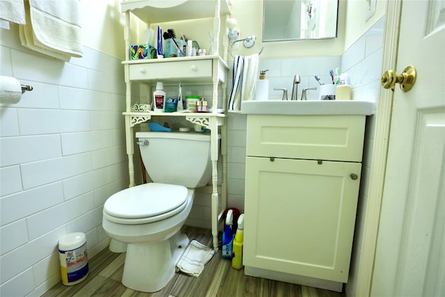 half bath with tile walls, vanity, toilet, and wood finished floors
