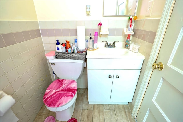 half bath with toilet, tile walls, wood finished floors, and vanity