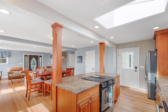 kitchen with freestanding refrigerator, decorative columns, range with electric stovetop, light stone counters, and light wood-style flooring
