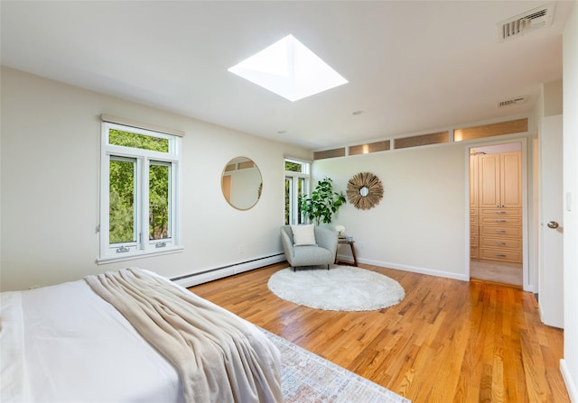 bedroom featuring a baseboard radiator, a skylight, multiple windows, and wood finished floors
