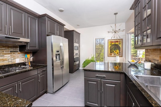 kitchen featuring stainless steel appliances, under cabinet range hood, decorative backsplash, light tile patterned floors, and dark stone counters