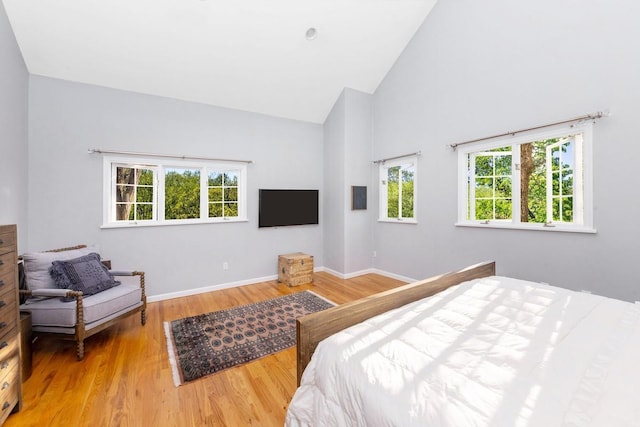 bedroom with wood finished floors, high vaulted ceiling, and baseboards
