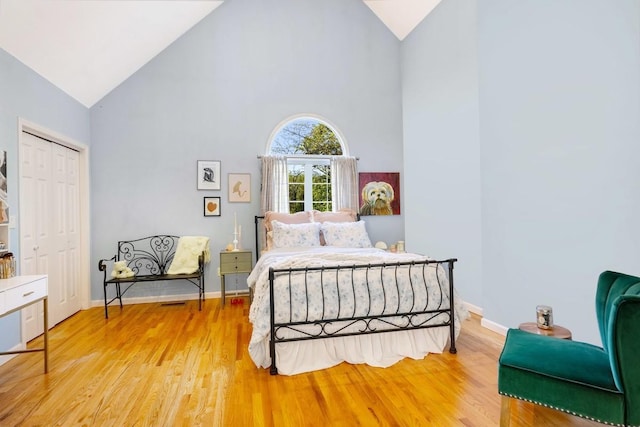 bedroom featuring high vaulted ceiling, light wood-style floors, baseboards, and a closet