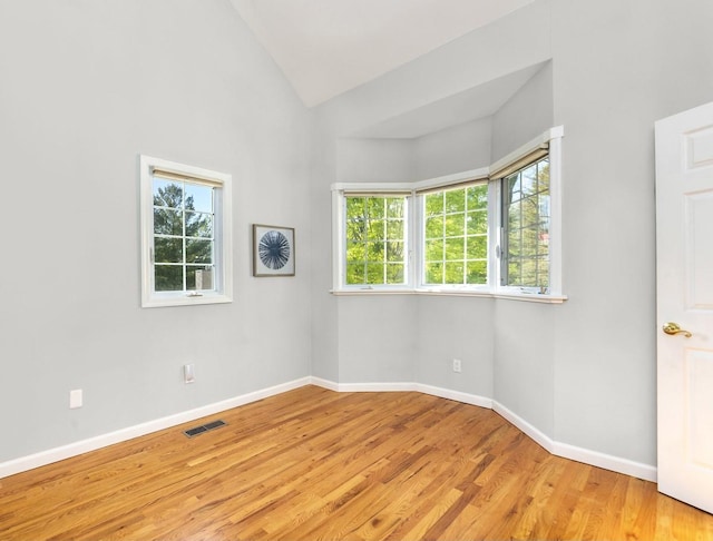 spare room featuring plenty of natural light, light wood finished floors, baseboards, and high vaulted ceiling