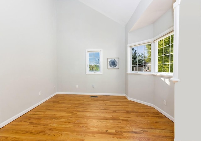 spare room with vaulted ceiling, light wood-style floors, and baseboards