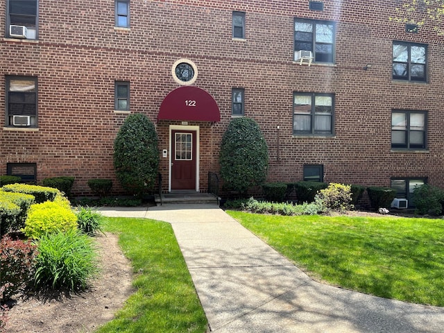 doorway to property featuring cooling unit, a yard, and brick siding