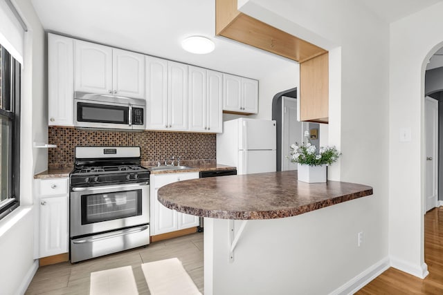 kitchen with baseboards, arched walkways, dark countertops, and stainless steel appliances
