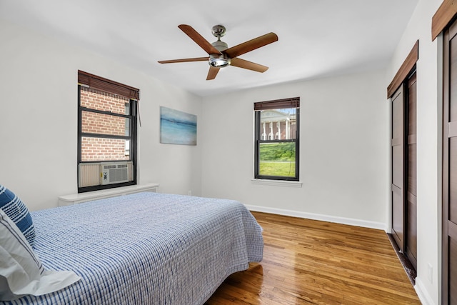 bedroom featuring a ceiling fan, baseboards, wood finished floors, and cooling unit