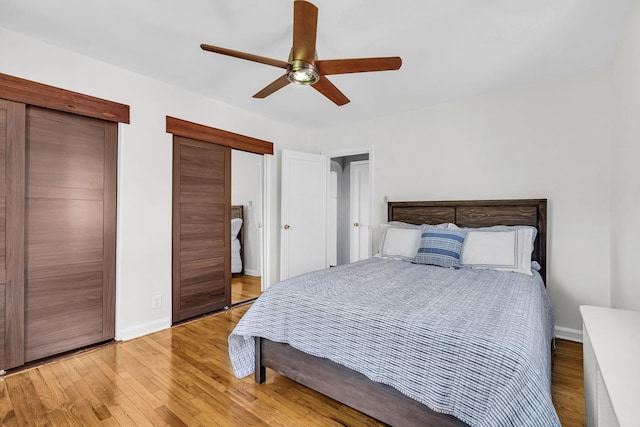 bedroom with baseboards, a ceiling fan, two closets, and wood finished floors