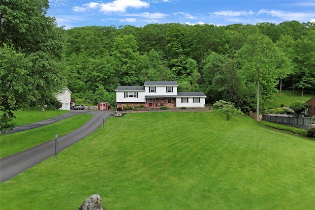 view of front of home featuring an outbuilding, a front lawn, a wooded view, fence, and brick siding
