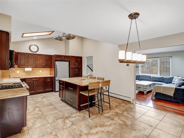 kitchen featuring stainless steel refrigerator, a sink, a baseboard heating unit, decorative backsplash, and open floor plan