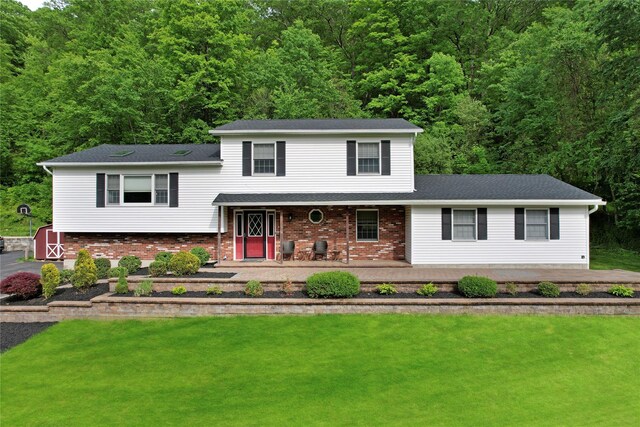 tri-level home featuring a porch, a view of trees, brick siding, and a front yard