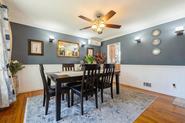 dining space with a wall mounted air conditioner, a wainscoted wall, a ceiling fan, wood finished floors, and visible vents