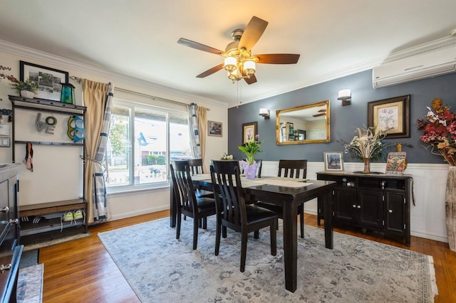 dining room featuring ceiling fan, a wall unit AC, crown molding, wainscoting, and wood finished floors