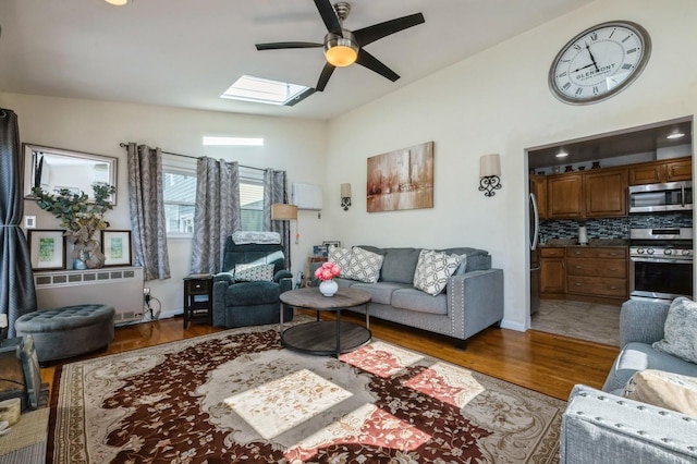 living area featuring radiator, a ceiling fan, baseboards, wood finished floors, and lofted ceiling with skylight