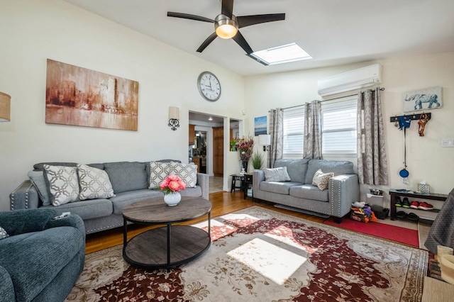 living room featuring ceiling fan, an AC wall unit, lofted ceiling with skylight, and wood finished floors