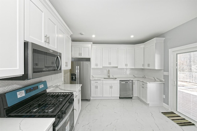 kitchen featuring appliances with stainless steel finishes, baseboards, white cabinetry, and a sink