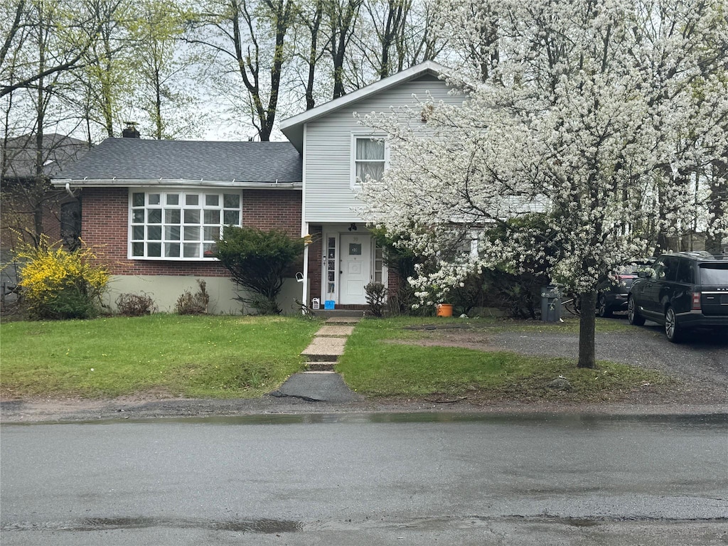 split level home featuring a chimney, a front yard, and brick siding