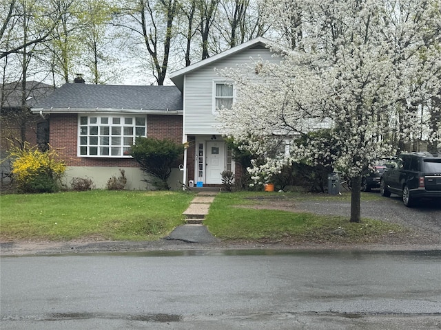 split level home featuring a chimney, a front yard, and brick siding
