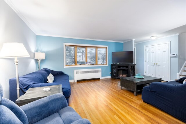 living room with radiator, baseboards, crown molding, and light wood finished floors