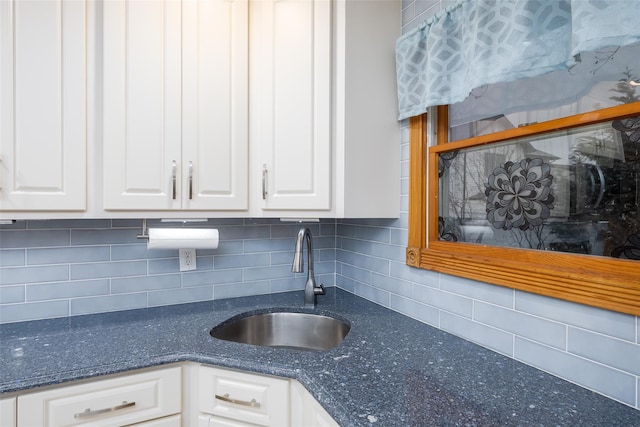 kitchen with decorative backsplash, dark stone countertops, a sink, and white cabinets