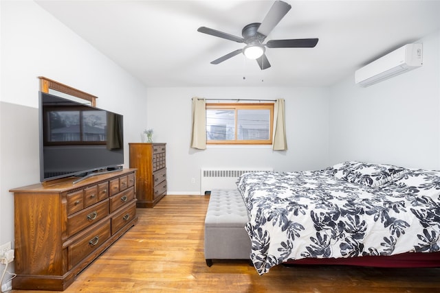 bedroom with a ceiling fan, radiator heating unit, light wood-style floors, baseboards, and a wall unit AC