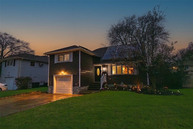 split level home with stone siding, driveway, a front yard, and a garage