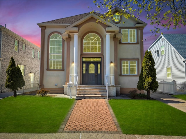 view of front facade featuring a lawn, stucco siding, and fence